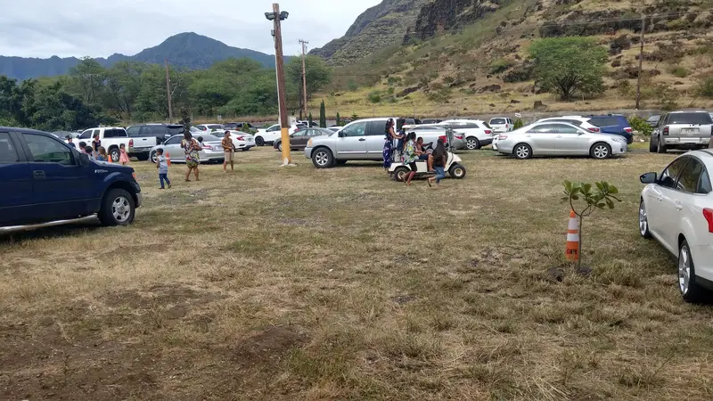 A wide grass parking field full of cars and families under the Waianae Range